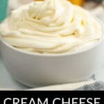A white bowl filled with swirled cream cheese whipped cream sits in focus, while a blurred dessert and spoon appear in the background. Text reads, "Cream Cheese Whipped Cream.