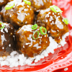 A plate of honey garlic meatballs over rice garnished with sesame seeds and green onions.