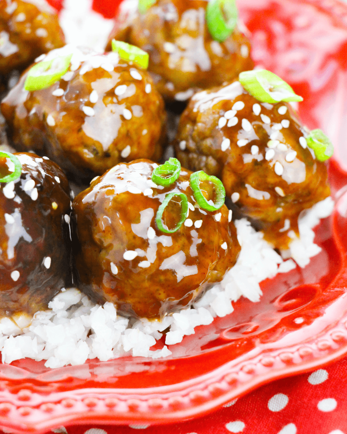 A plate of honey garlic meatballs over rice garnished with sesame seeds and green onions.