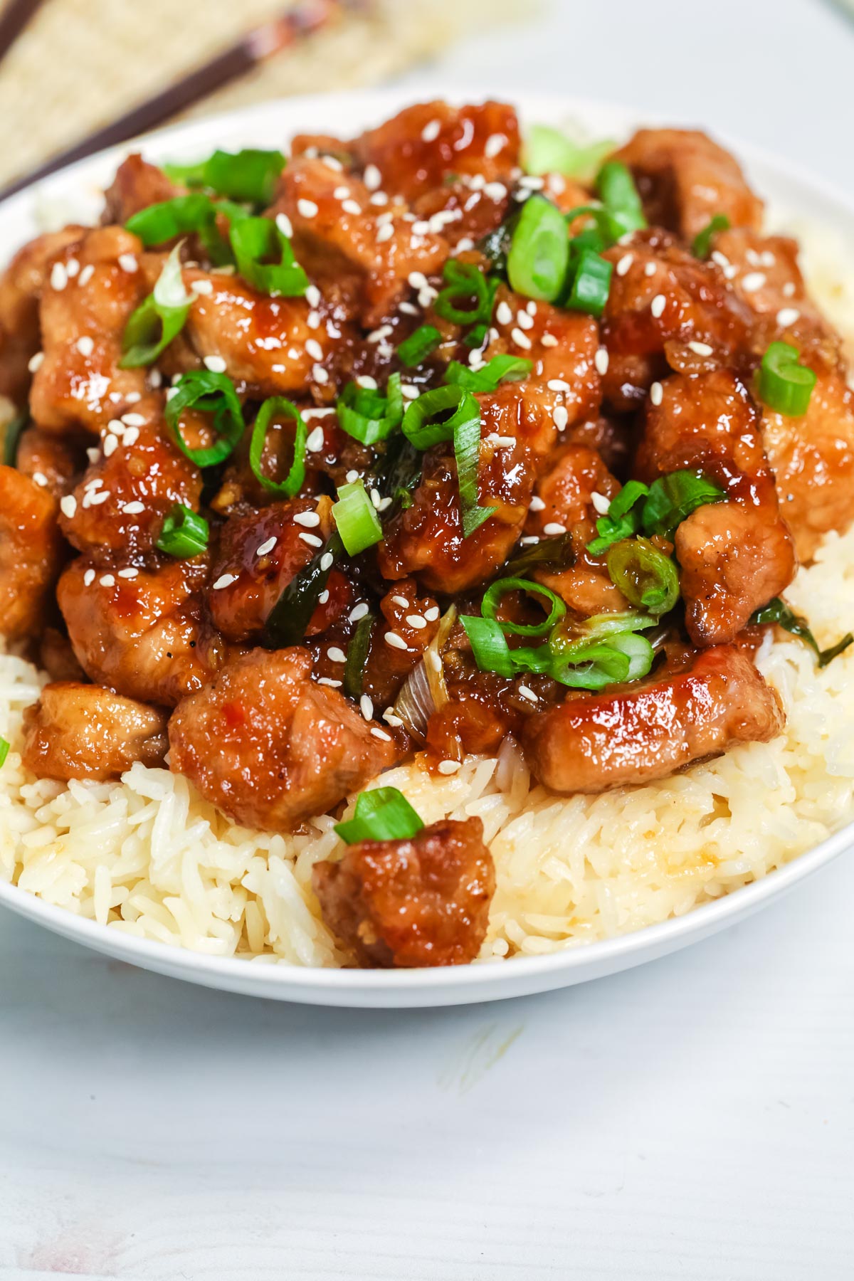 Mongolian pork atop a bowl of rice with green onions and sesame seeds on top.