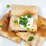 A plate of shredded chicken quesadillas topped with sour cream, chopped green onions, and cilantro.