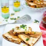 A plate of shredded chicken quesadillas topped with sour cream and cilantro sits elegantly on a white plate, while bottles of mineral water and a tempting stack of more quesadillas await in the background.