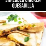 A mouthwatering close-up of shredded chicken quesadilla slices, perfectly topped with sour cream and a sprinkle of fresh cilantro, invites you to indulge in this flavorful delight.