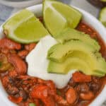 A bowl topped with avocado slices, lime wedges, and a dollop of sour cream.