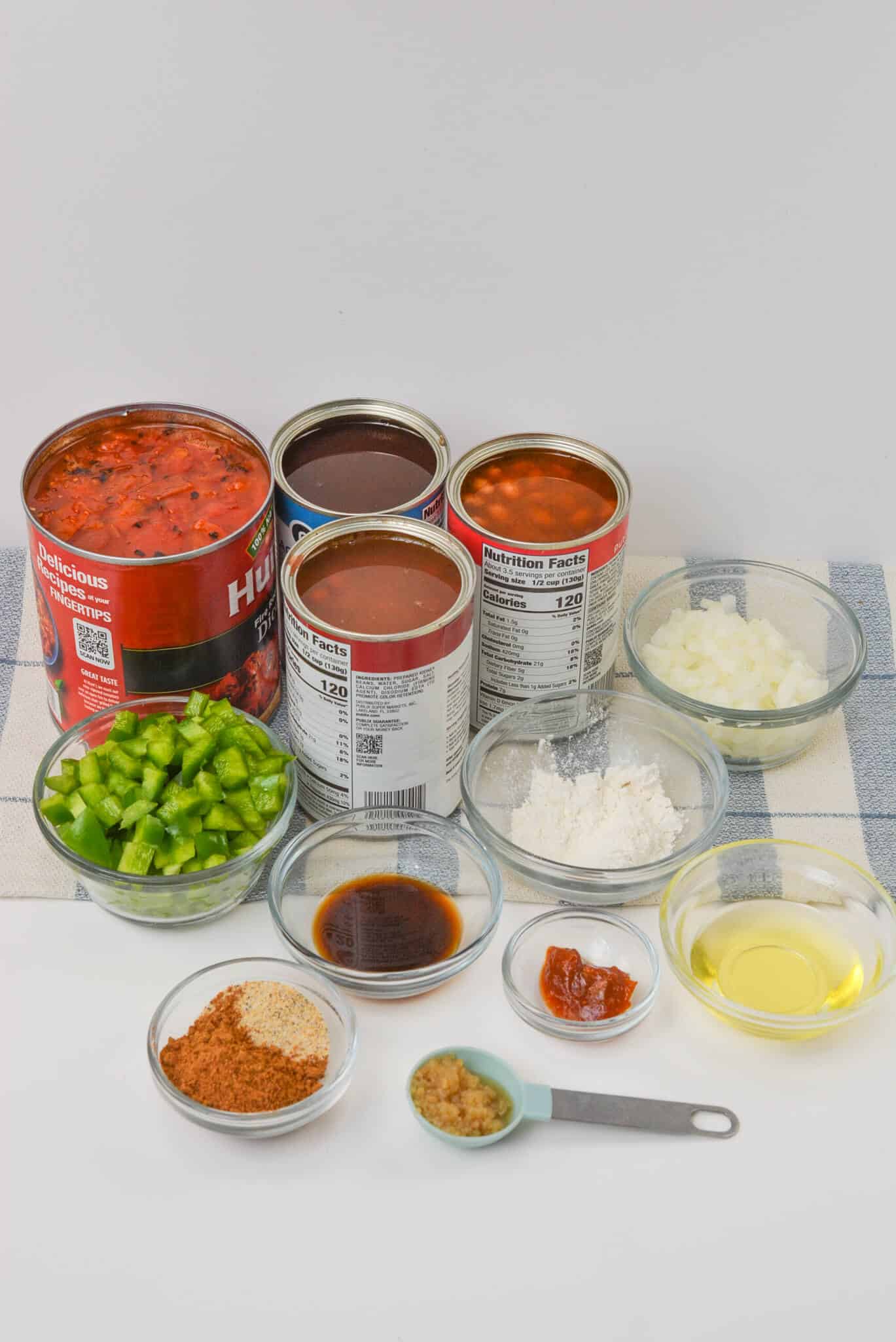 Assorted ingredients including canned tomatoes, beans, diced green peppers, chopped onions, and various spices, arranged on a white surface.