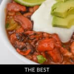 A hearty bowl of flavorful three-bean chili, artfully topped with a dollop of sour cream, creamy avocado slices, and tangy lime wedges.