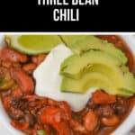 A bowl of savory three bean chili, crowned with fresh avocado slices and a dollop of sour cream.