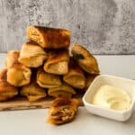 Buffalo chicken egg rolls served on a wooden board with a side of dipping sauce.