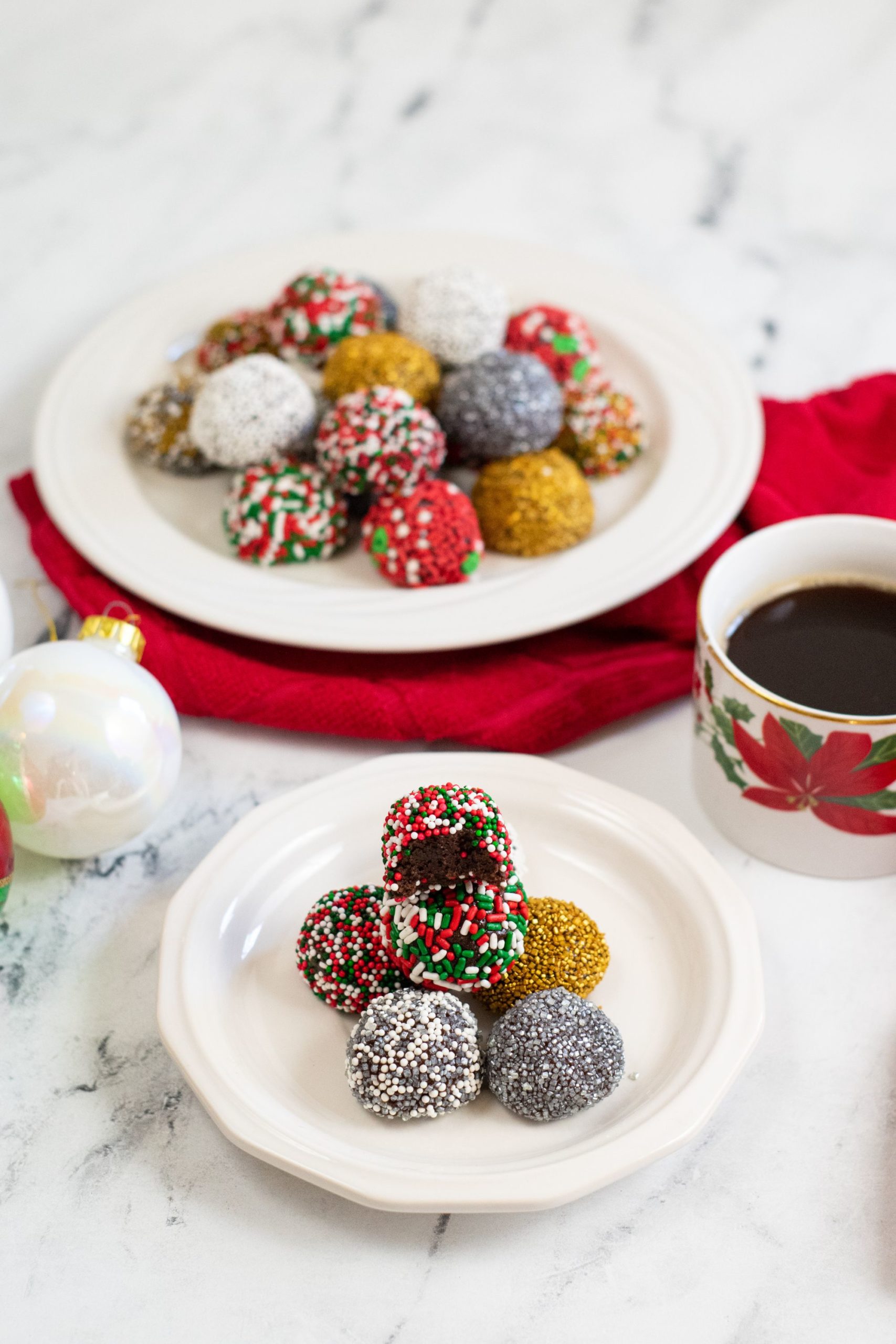 Brownie balls coated in sprinkles and piled on a white plate with a cup of coffee off to the side