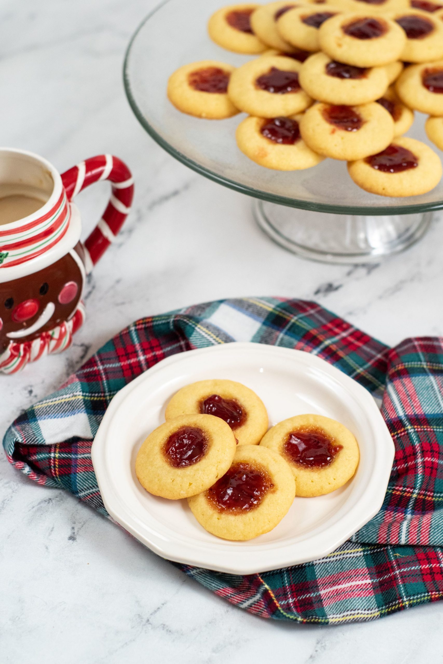 Jam thumbprint cookies on a white plate with a plaid napkin
