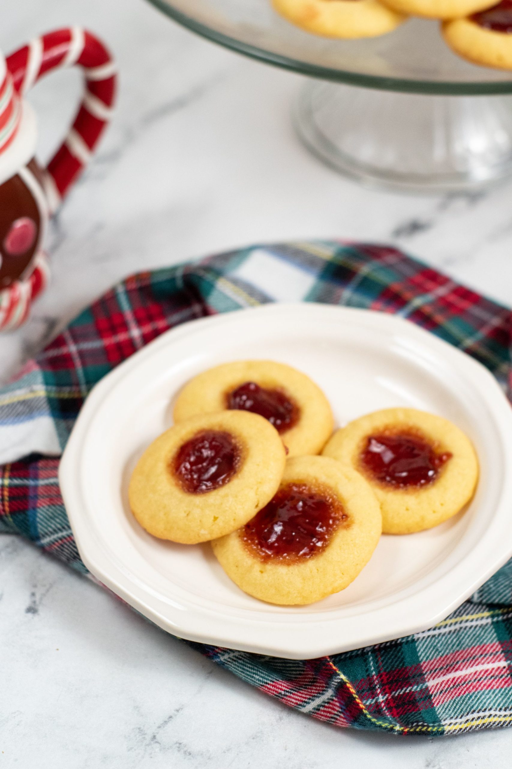 old fashioned thumbprint cookies on a white plate with a plaid napkin
