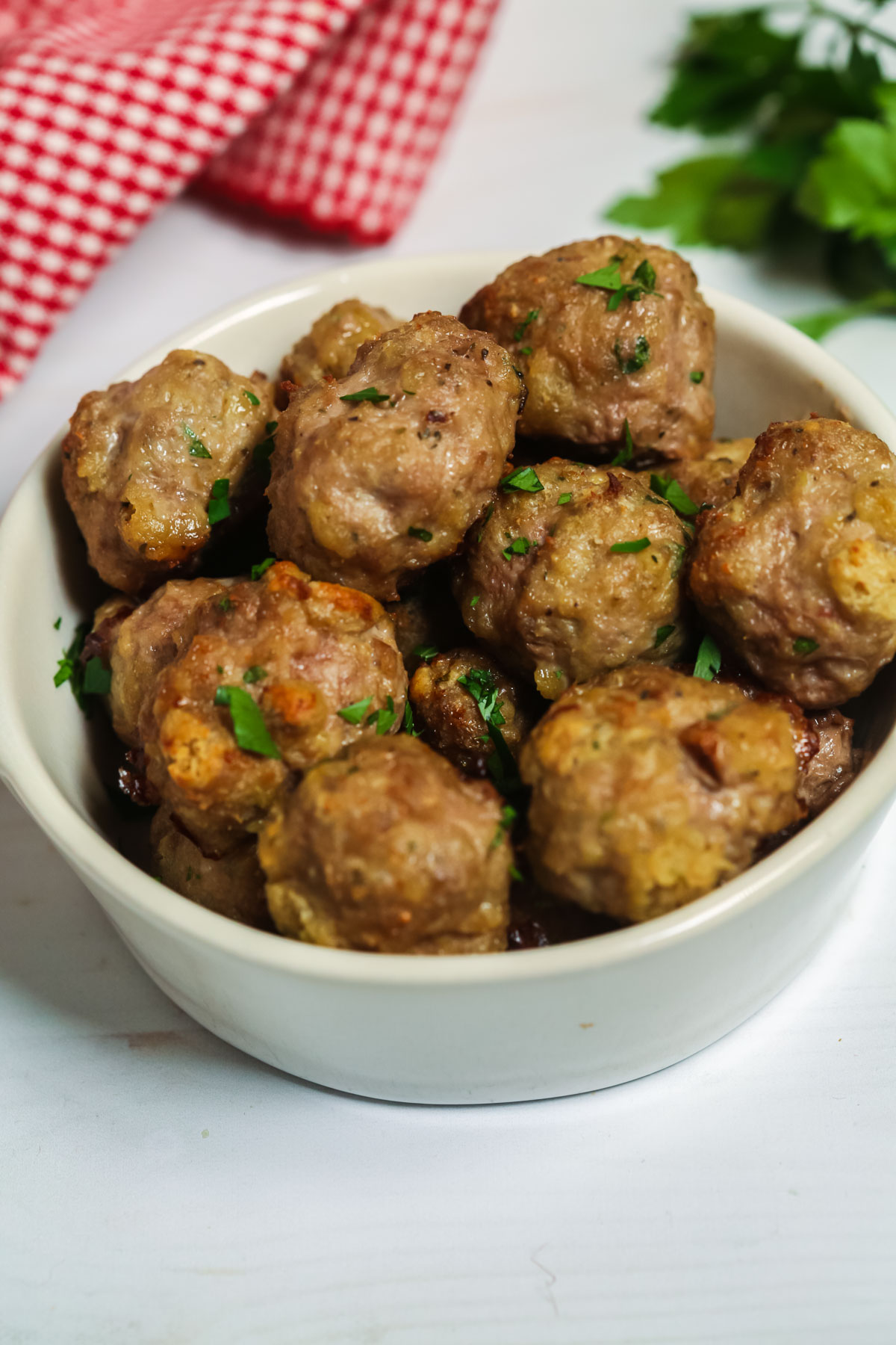 Oven baked meatballs in a white bowl with parsley flakes. 