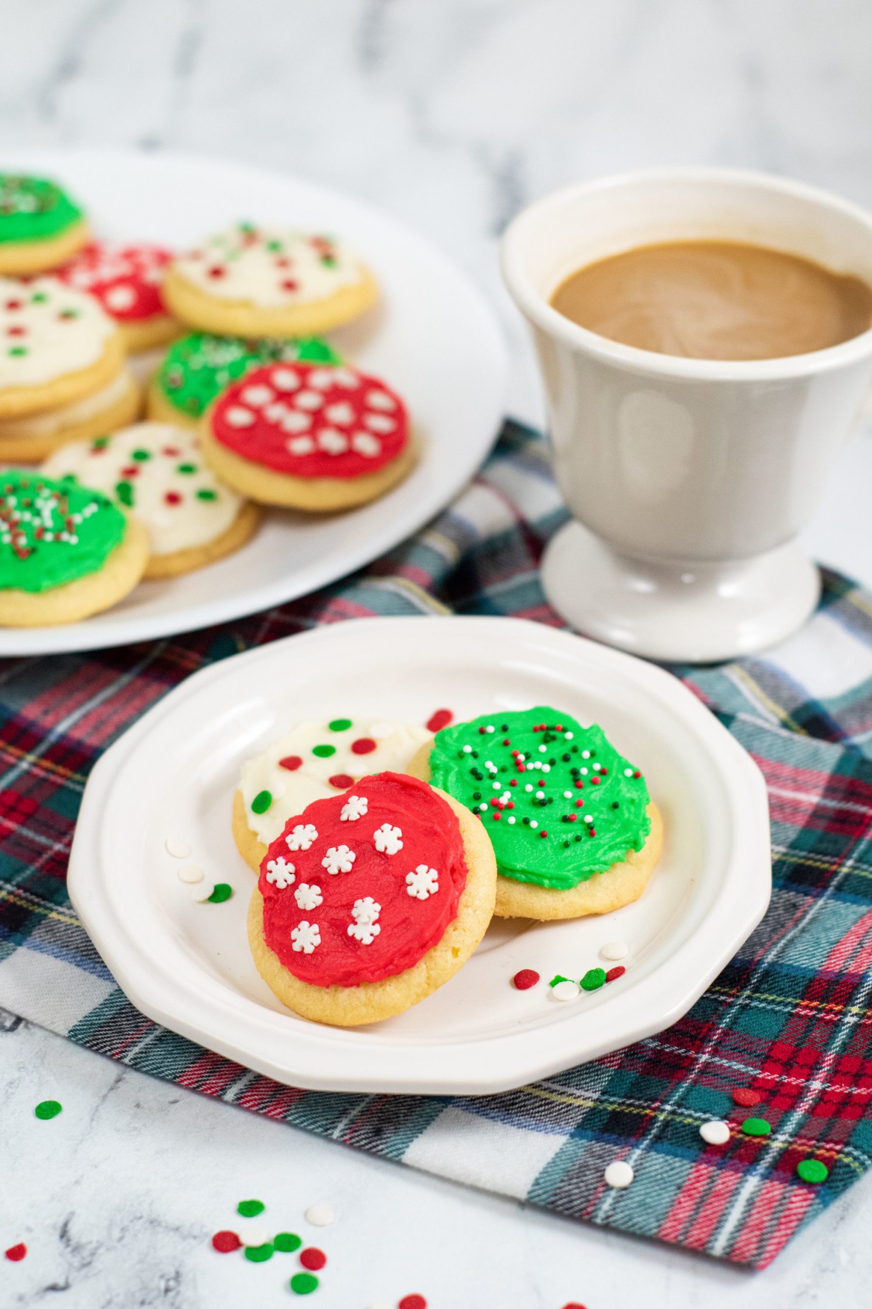 soft frosted cookies on a white plate with a cup of coffee in the background