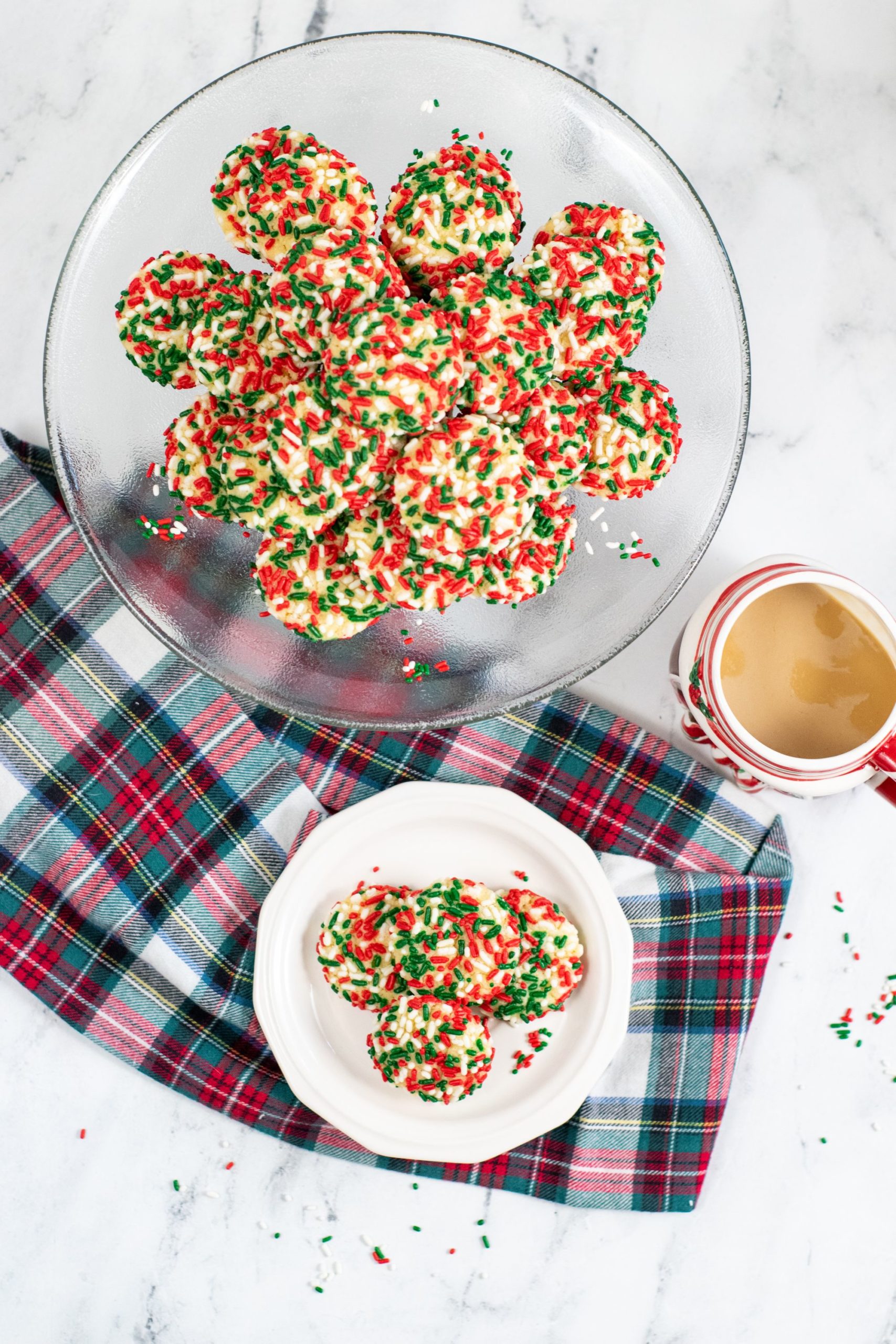 christmas sugar cookies with sprinkles on a plate with a plaid napkin.