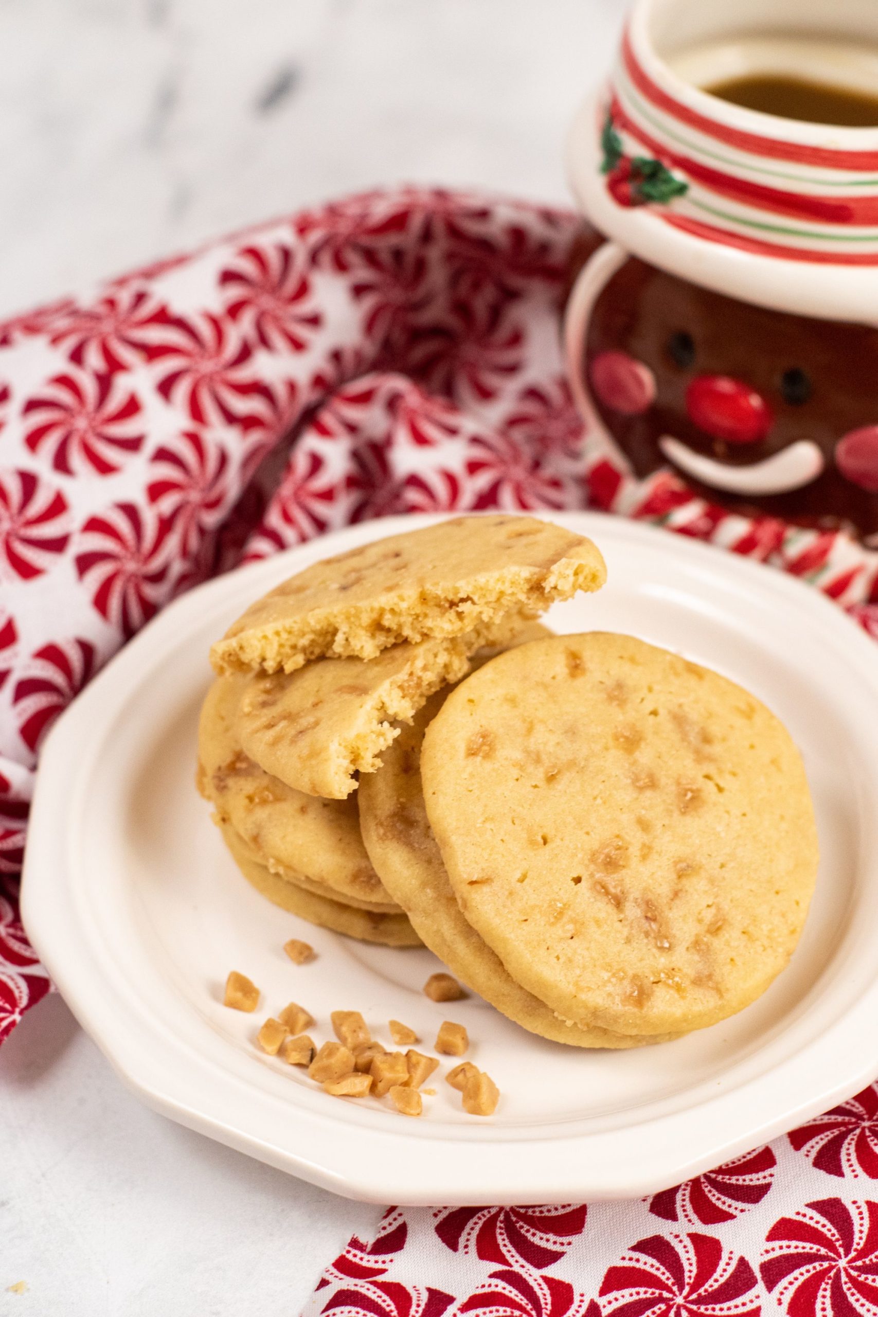 Toffee cookies in a pile on a white plate with a gingerbread mug in the background