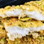 Piece of white fish showing the inside of fish and the pistachio crust on top.