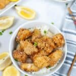 A bowl of the chinese lemon chicken with lemon wedges on the side.