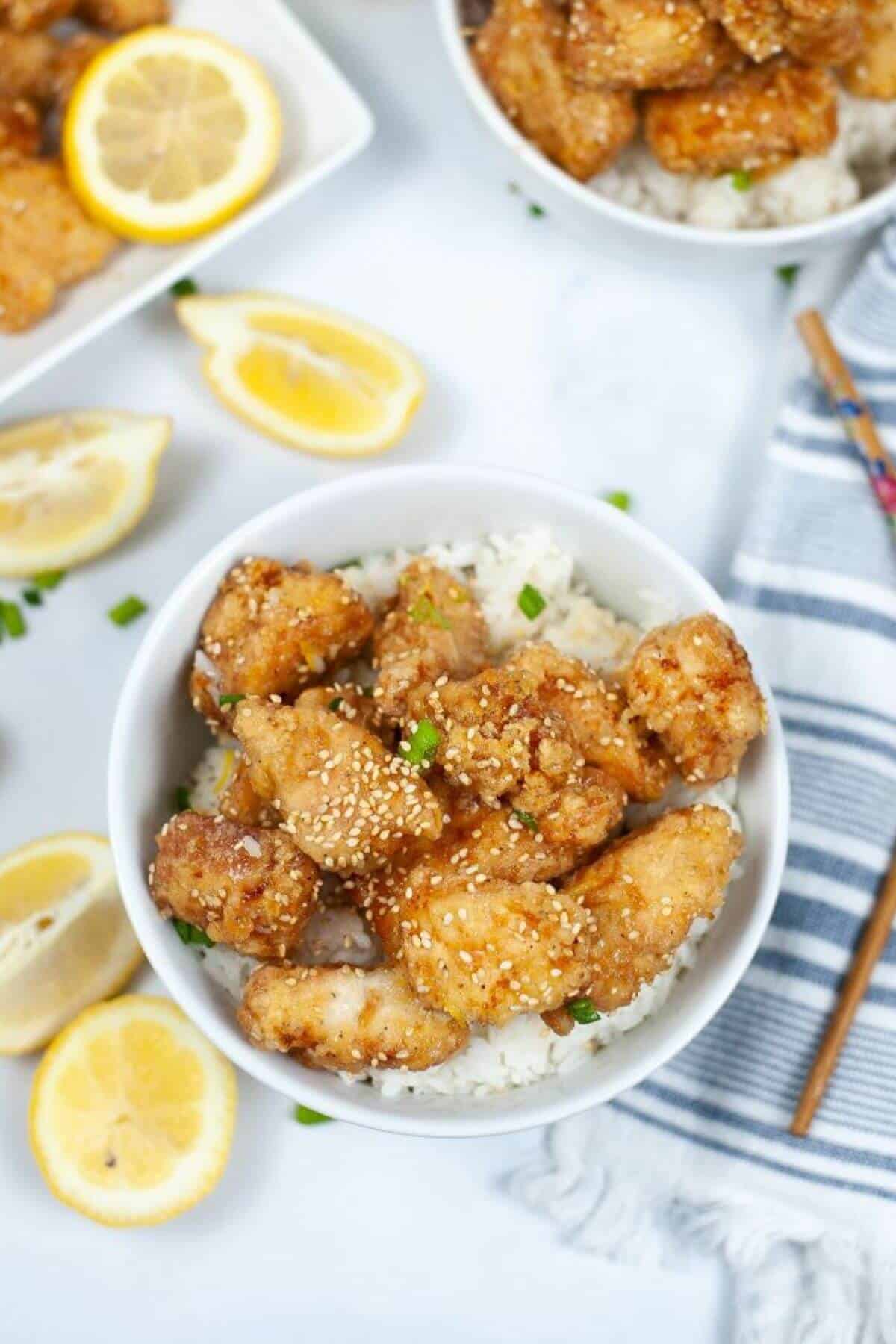 A bowl of the chinese lemon chicken with lemon wedges on the side.