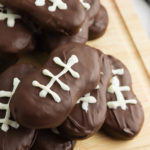 Football cookies stacked on a wooden cutting board.