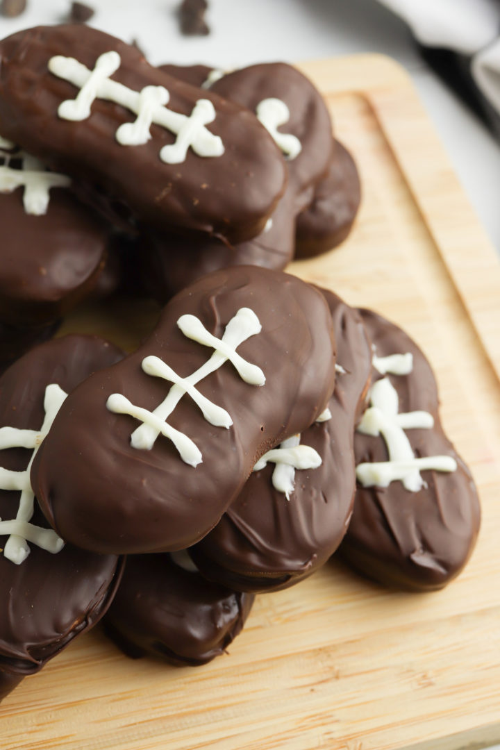 Football cookies stacked on a wooden cutting board.