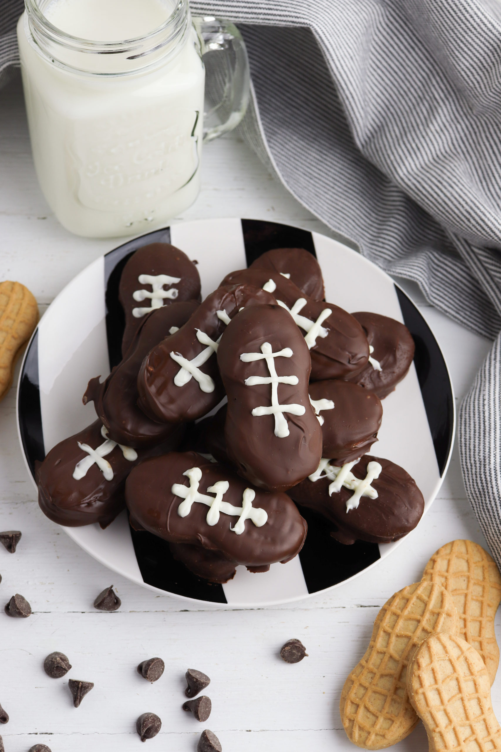 White platter of football cookies with chocolate chips and milk on the side.