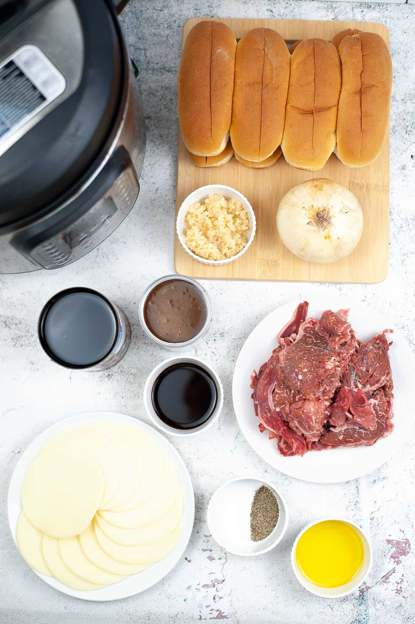 Ingredients for a beef sandwich, including rolls, raw beef, onion, garlic, sauces, cheese slices, and spices arranged on a light surface next to an Instant Pot for a delicious French Dip.