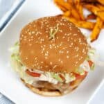 A sesame seed hamburger with lettuce, tomato, and cheese on a white plate, served with a side of sweet potato fries—try our Instant Pot Teriyaki Chicken Sandwich for a flavorful twist.