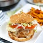A cheeseburger with lettuce, tomato, and melted cheese on a sesame seed bun sits on a white plate next to a serving of sweet potato fries, sharing the spotlight with our flavorful Instant Pot Teriyaki Chicken Sandwich.