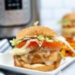 A sub on a plate with melted cheese, lettuce, tomato, and onions on a sesame bun sits on a white plate, with an Instant Pot in the background.