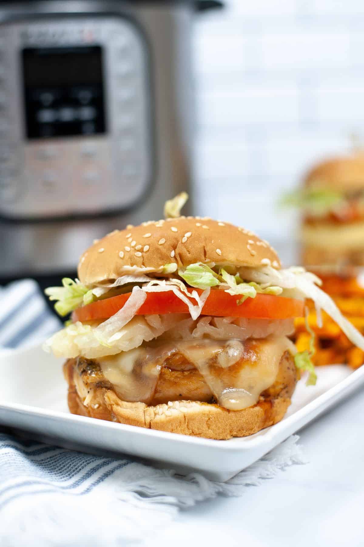 A sub on a plate with melted cheese, lettuce, tomato, and onions on a sesame bun sits on a white plate, with an Instant Pot in the background.