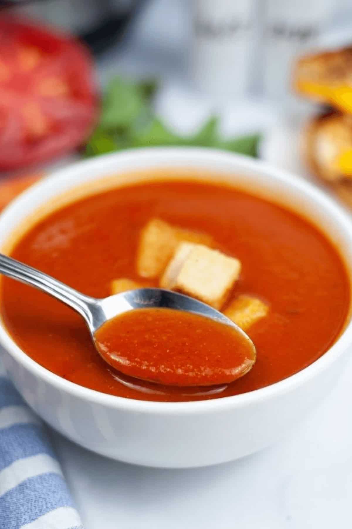 A bowl of the dish with a spoon in it and croutons on top.