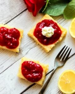Raspberry Lemonade Bars on a board one with whipped cream.