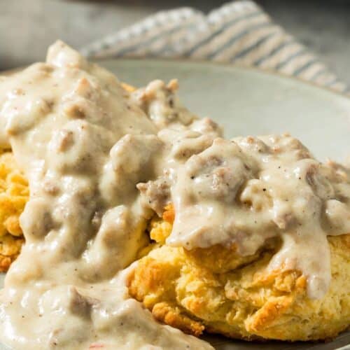A plate of sausage biscuits topped with creamy sausage gravy, served on a striped cloth napkin.