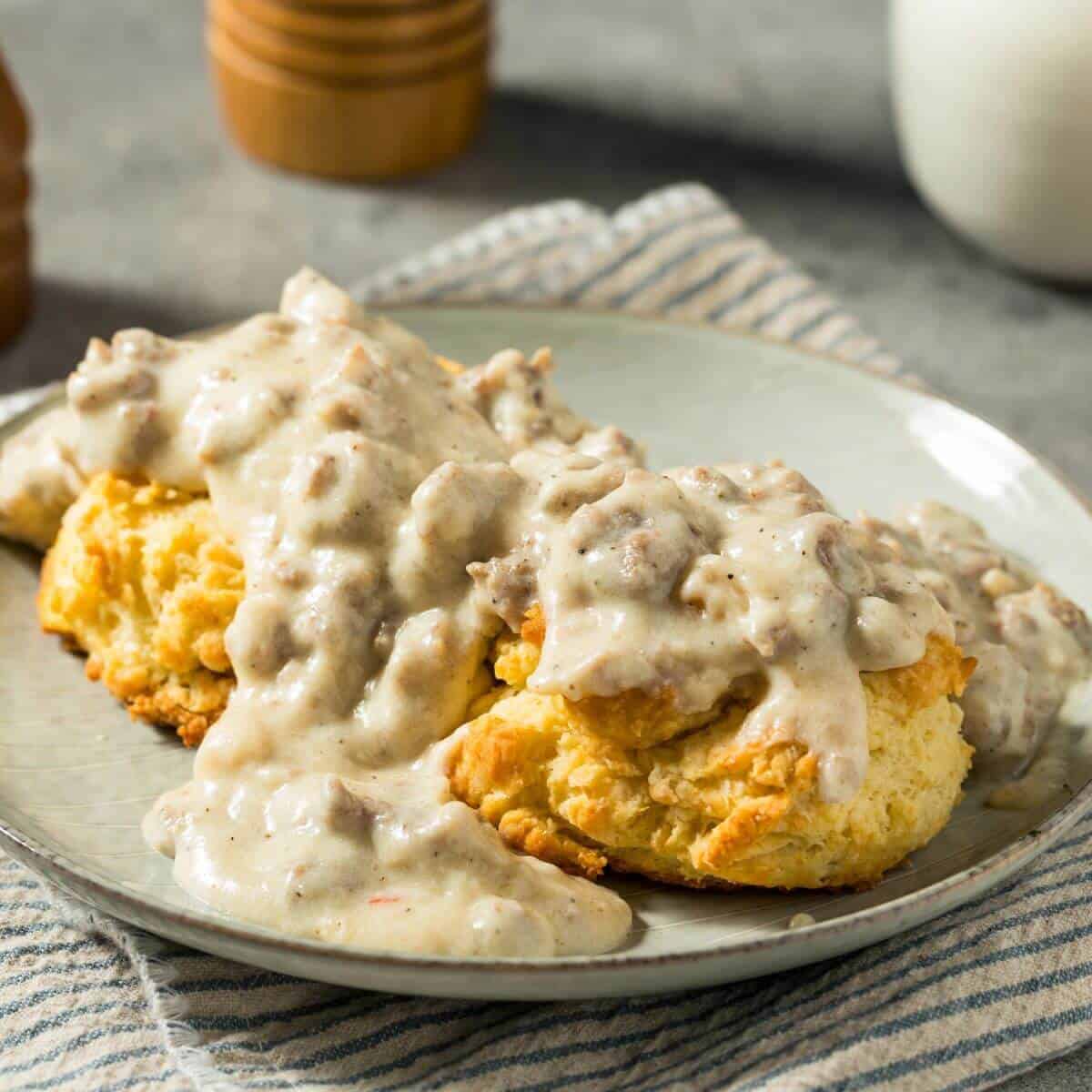 Two sausage biscuits topped with savory gravy are served on a plate, resting on a striped cloth.