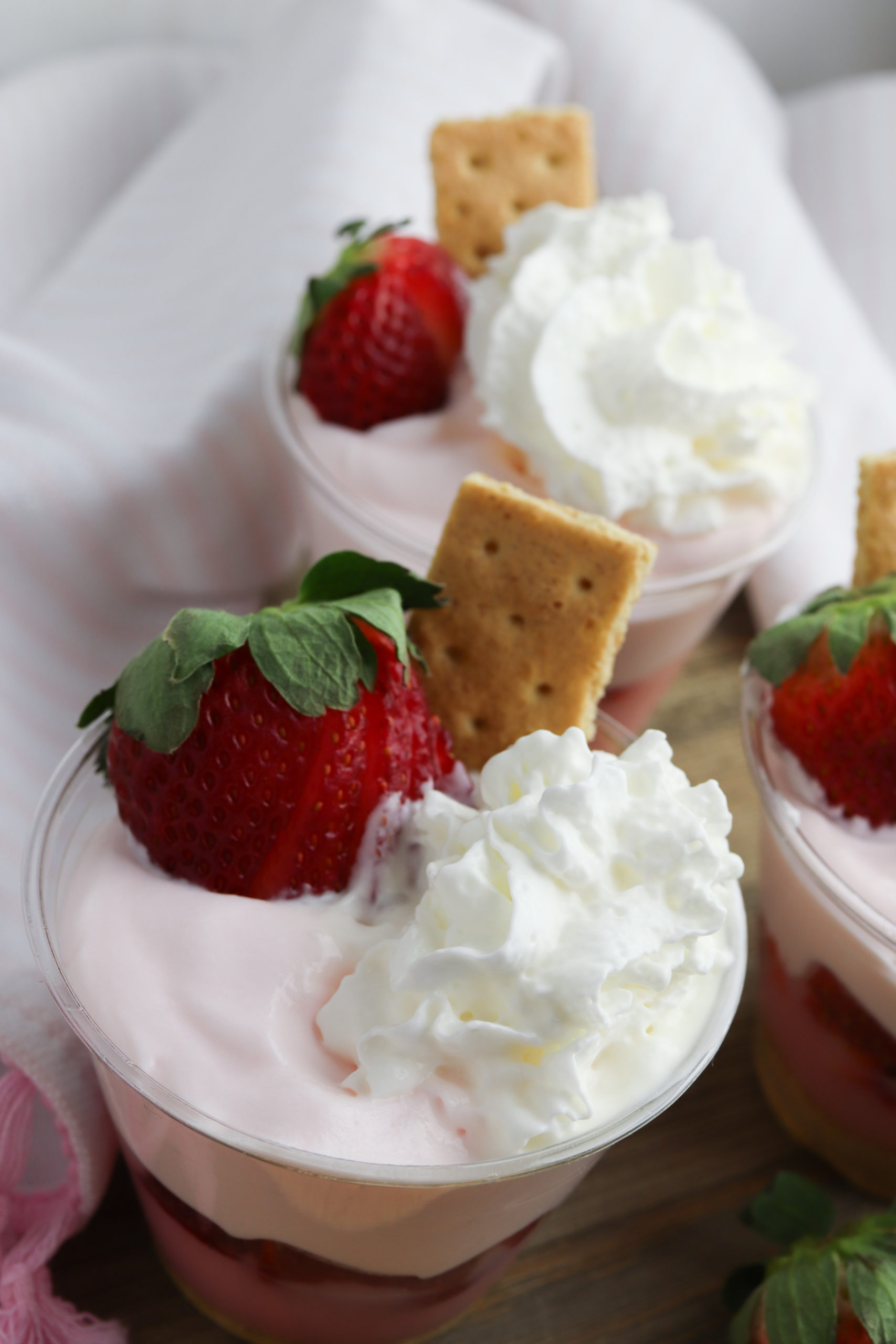 Strawberry Pudding Parfaits with whipped cream, a cookie and strawberry garnish.