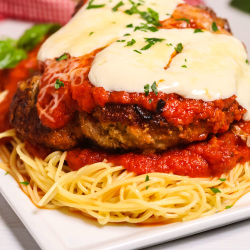 Veal Parm on a white square plate on top of spaghett.