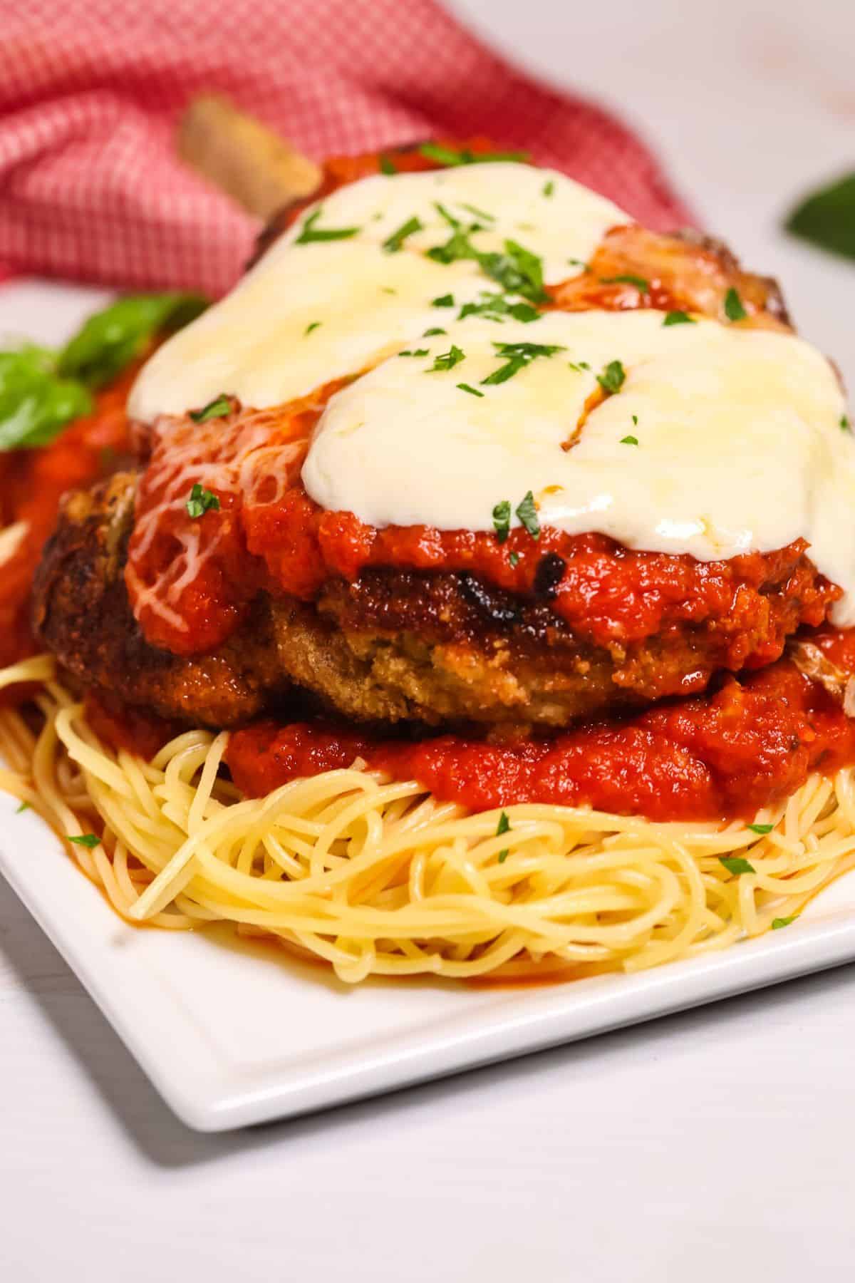 A plate of spaghetti topped with breaded veal cutlets, tomato sauce, and melted mozzarella cheese, reminiscent of classic Veal Parmesan, garnished with chopped parsley.