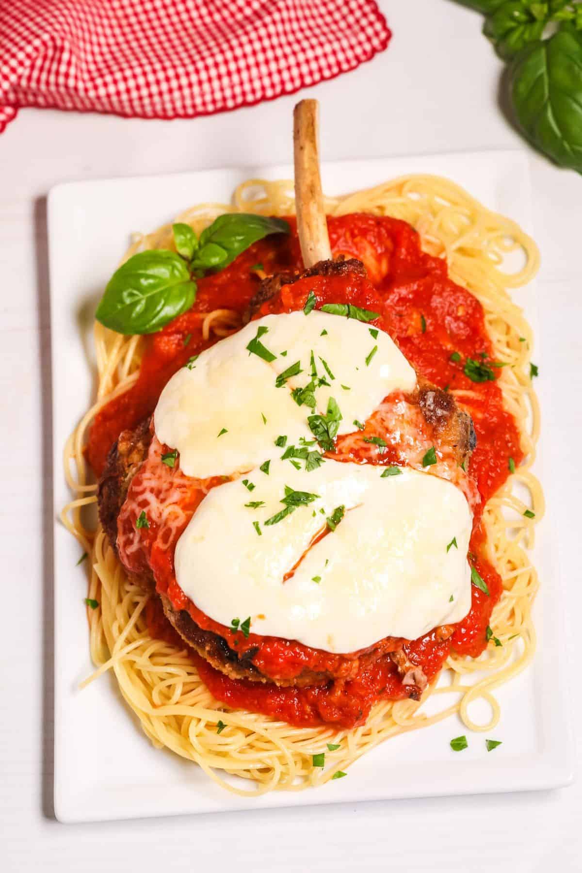 A classic chop topped with melted cheese and tomato sauce, served over a bed of spaghetti and garnished with chopped parsley and basil.