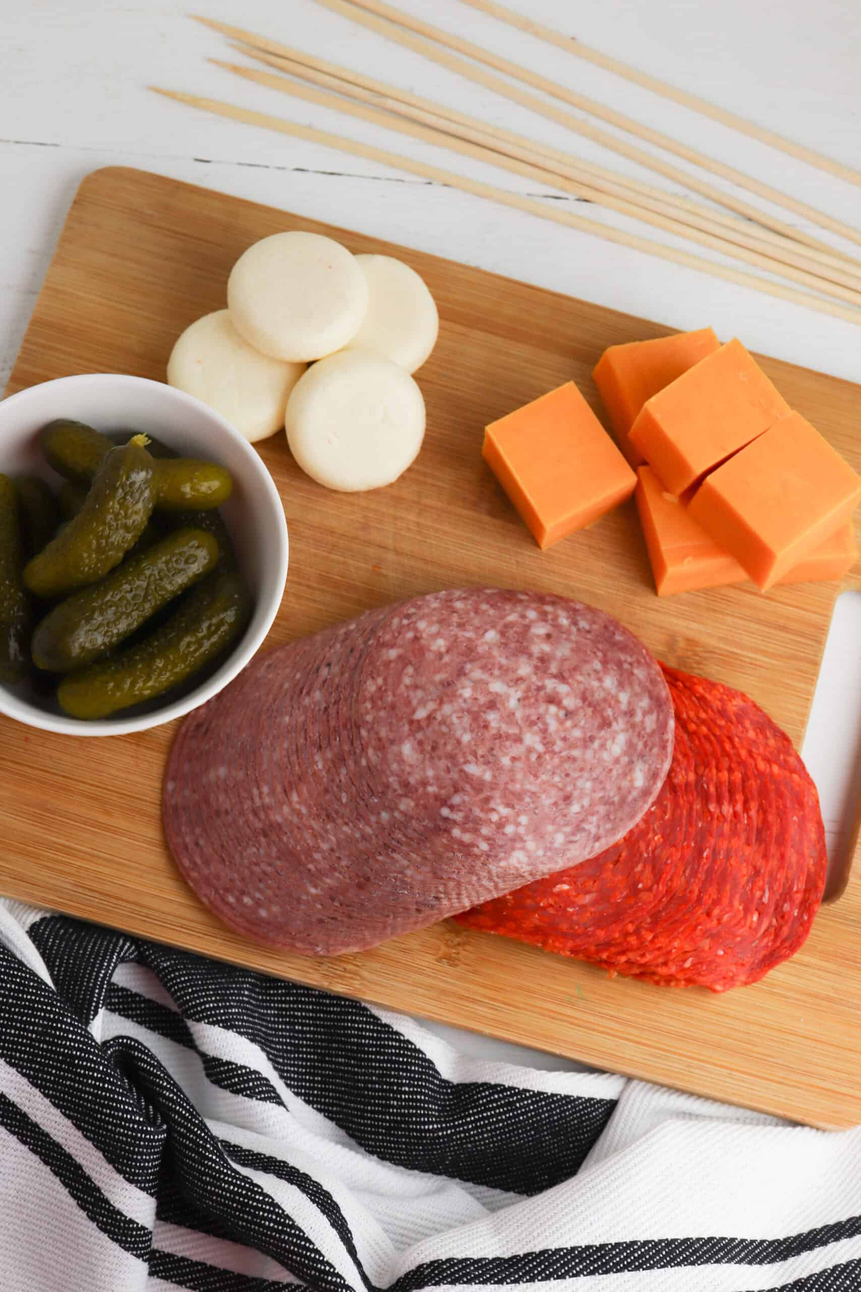 A wooden board with slices of salami, rounds of mozzarella, cheese cubes.