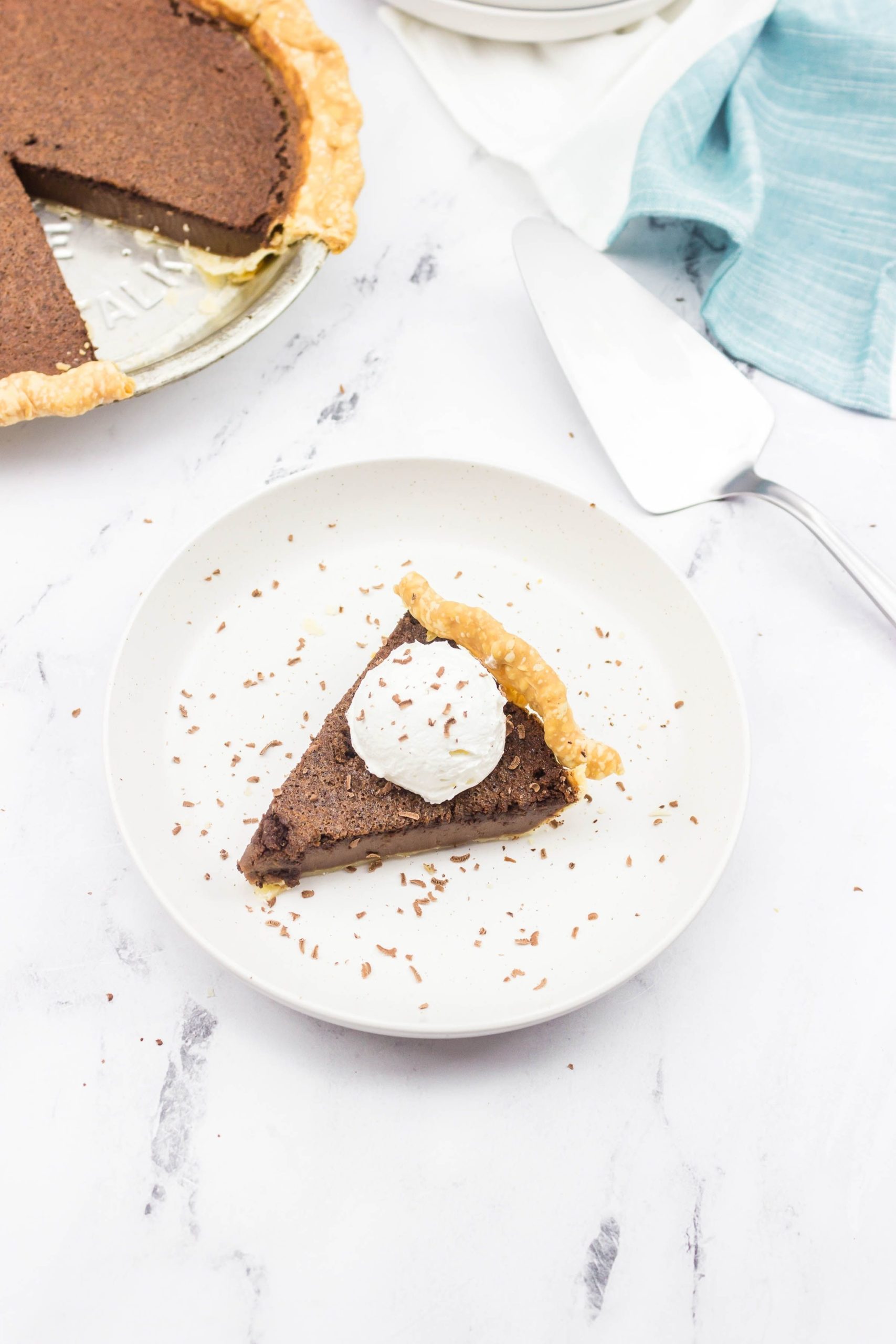  Chocolate Chess Pie on a white plate. With a server and a blue napkin on the side.