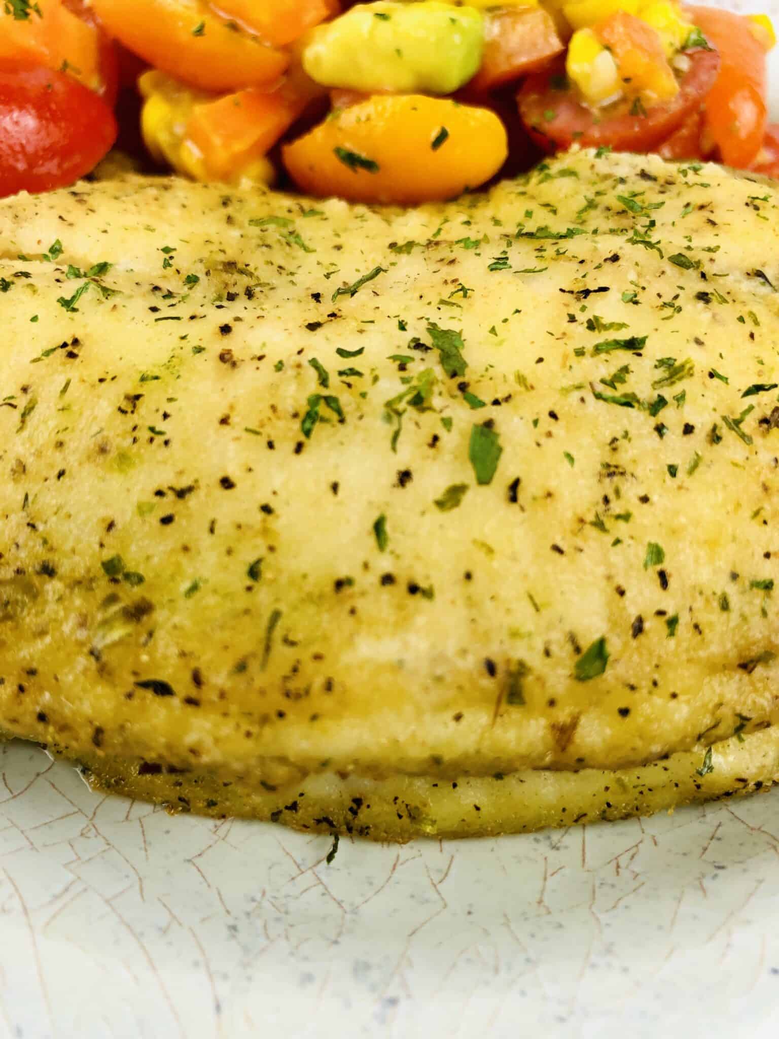 A close-up of a herb-seasoned fish with a side of mixed tomatoes and corn salad.