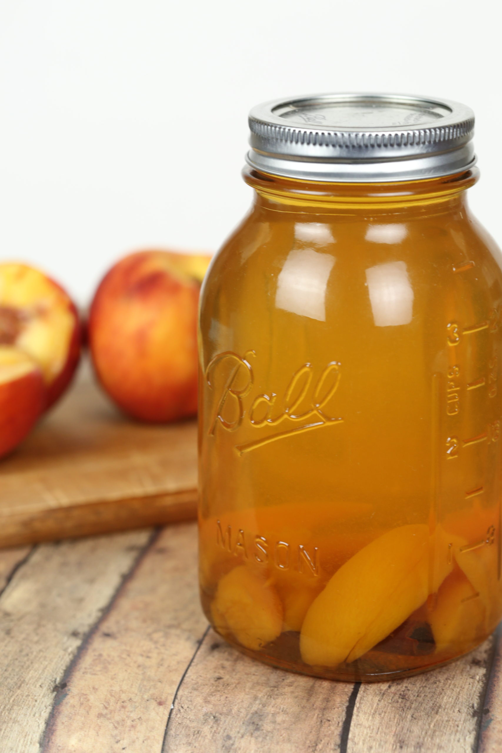 Peach Moonshine in a mason jar with peaches in the background.