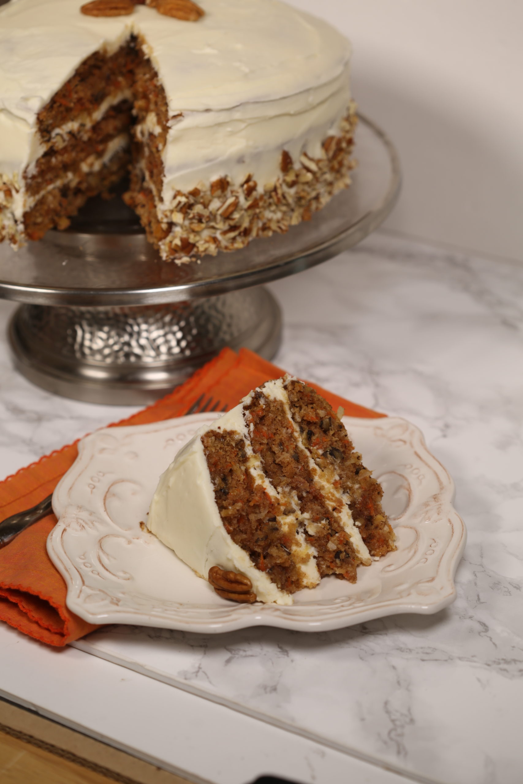The Ultimate Carrot Cake in a side view with the cake with a slice cut out in the background.