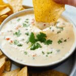 A person delicately dipping a tortilla into a bowl of white queso dip.