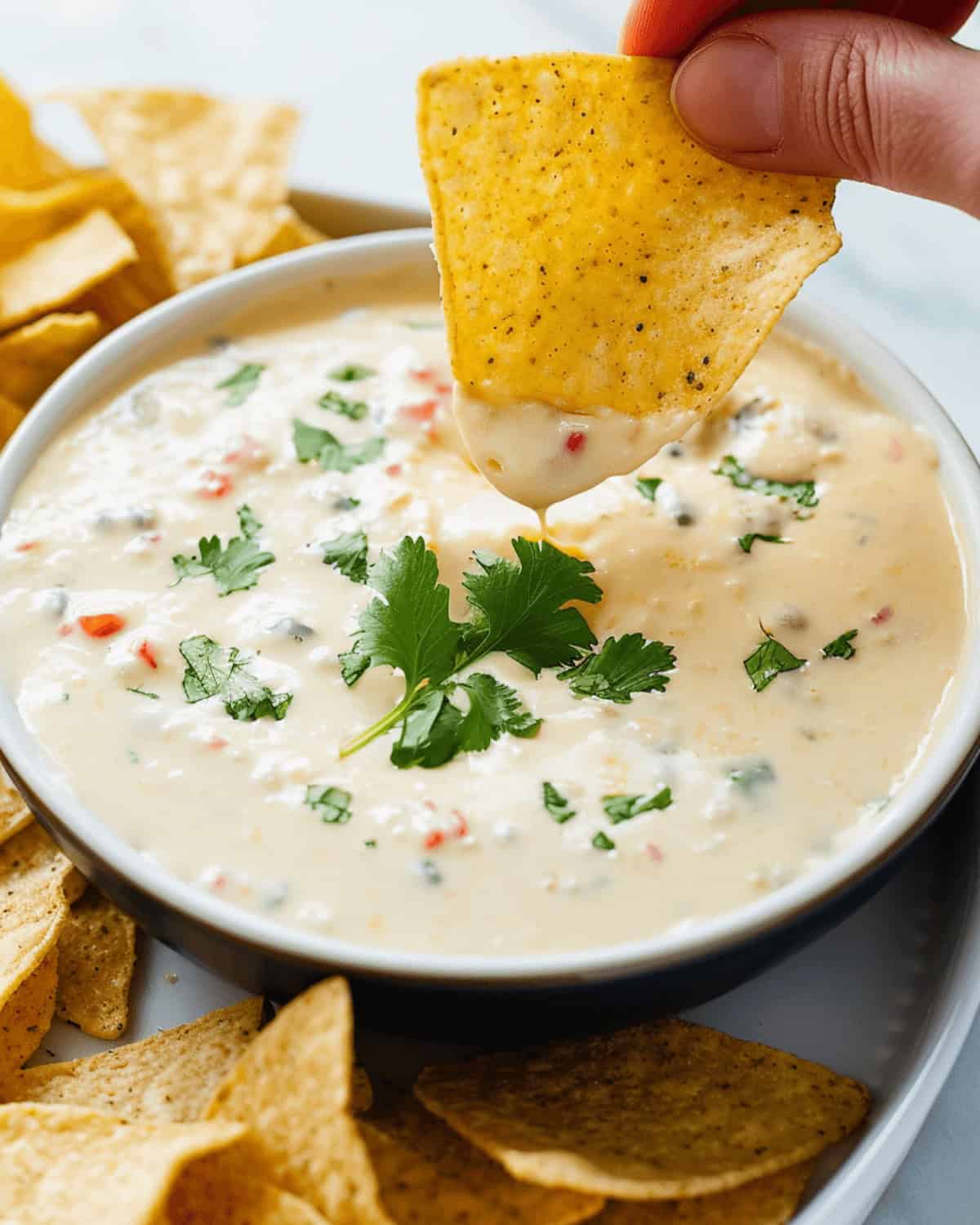 A person delicately dipping a tortilla into a bowl of white queso dip.