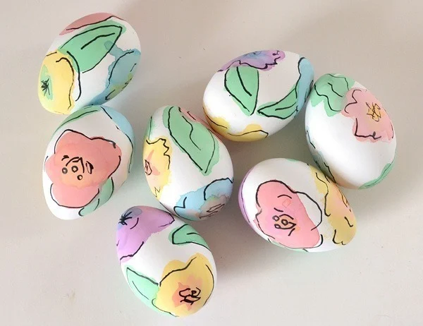 An assortment of white eggs decorated with watercolor painted flowers in the colors blue, purple, pink, green and yellow.