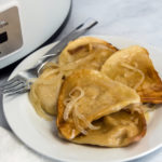 Crock Pot Pierogi on a white plate with a fork and knife. Aa crock pot can be seen in the background.