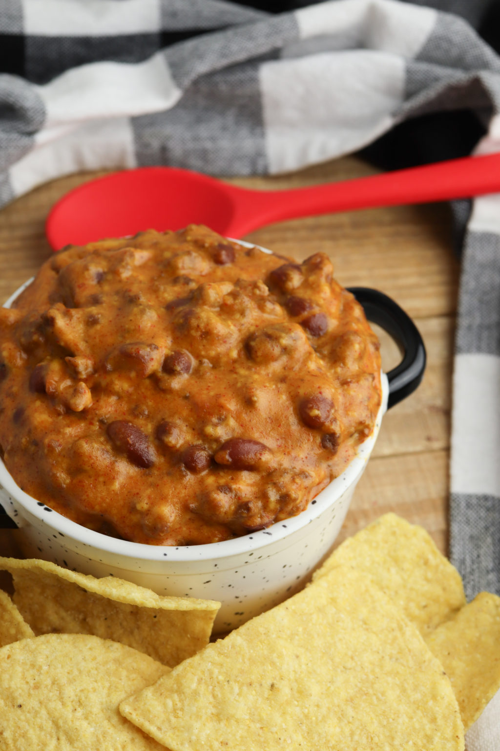 Crockpot Chili Cheese Dip with a spoon in the pot. A checked napkin on the side.