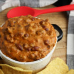 Crockpot Chili Cheese Dip with a spoon in the pot. A checked napkin on the side.