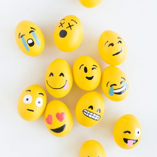 Eggs painted yellow with faces painted on them that represent a variety of emojis.